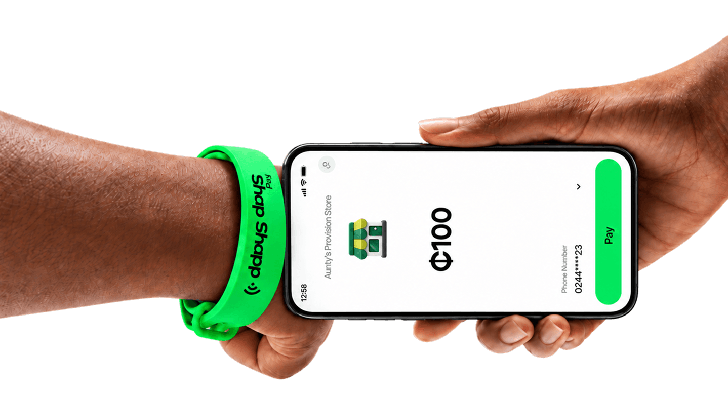 Hands holding a phone showing a ₵100 payment, with a green Shap Shapp band on the wrist